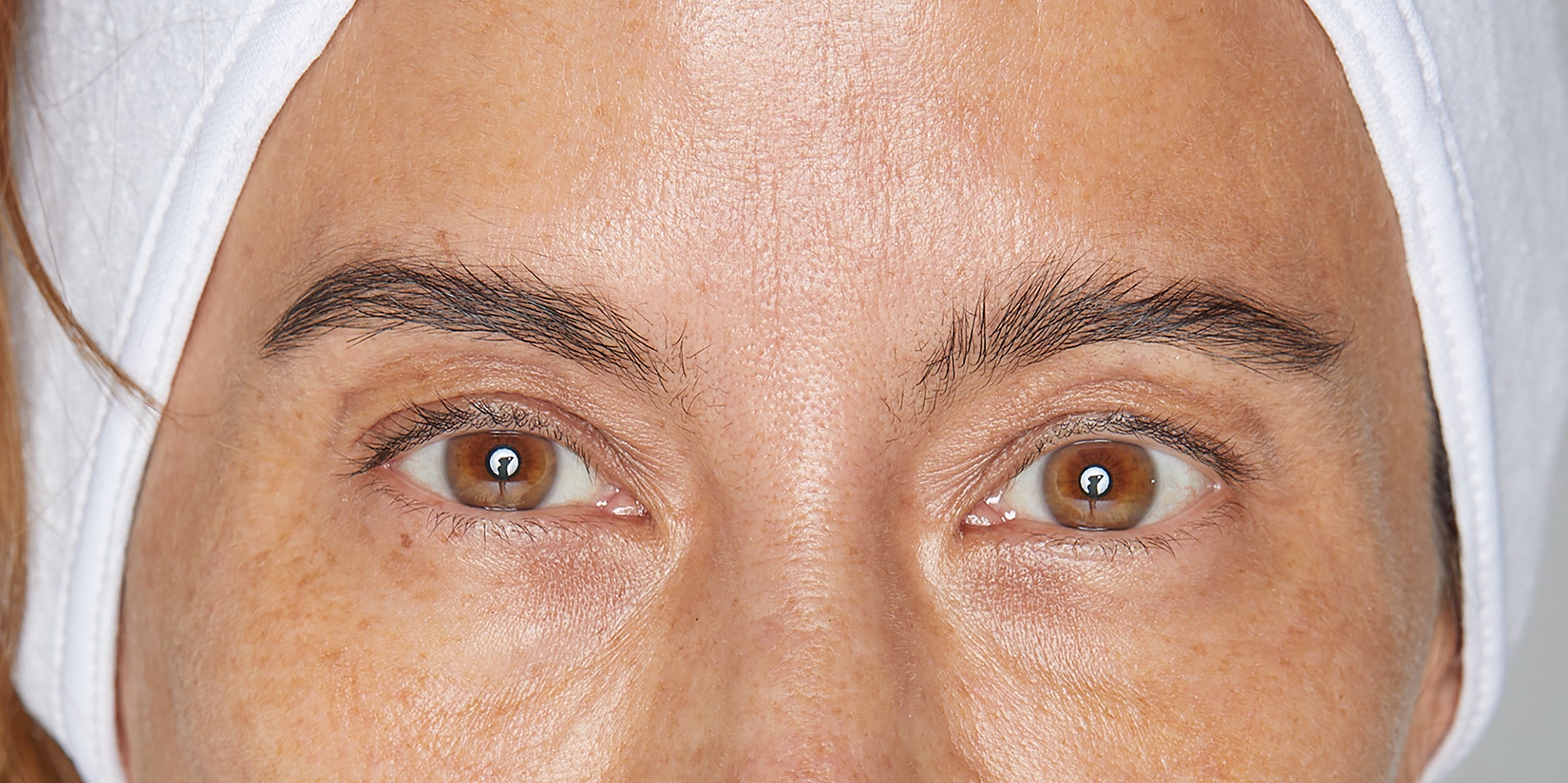 Brown eyes with freckled skin, visible pores and eyebrows, framed by a white headband.