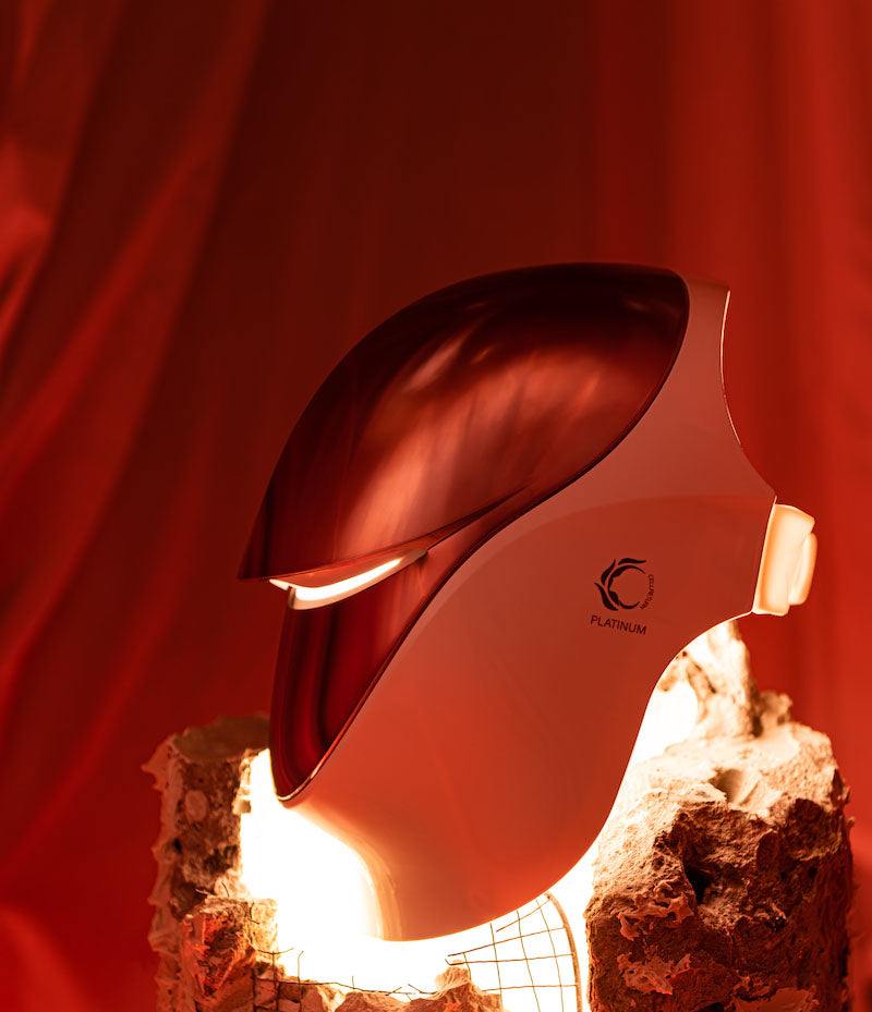 Futuristic white-and-red helmet with glossy red visor and PLATINUM logo, lit from below on a rough stone pedestal