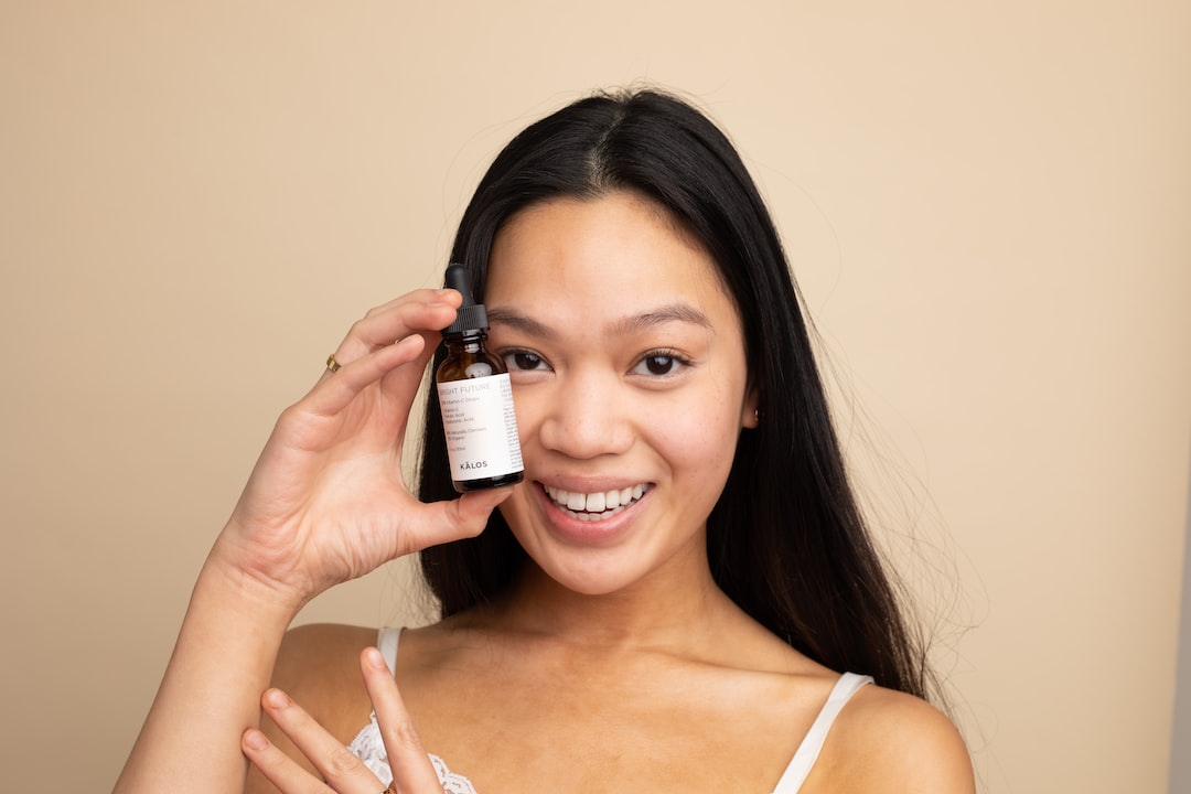 Smiling woman holding a dropper bottle labeled KALOS next to her right eye.